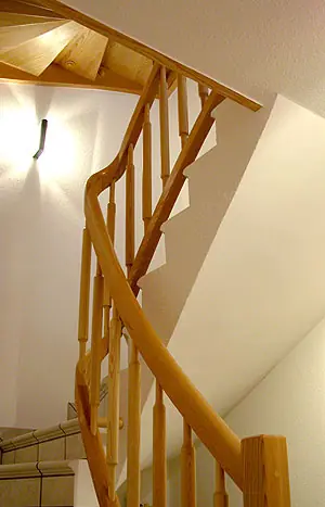 Holztreppe mit geschwungenem Handlauf und Geländerstäben im Treppenhaus